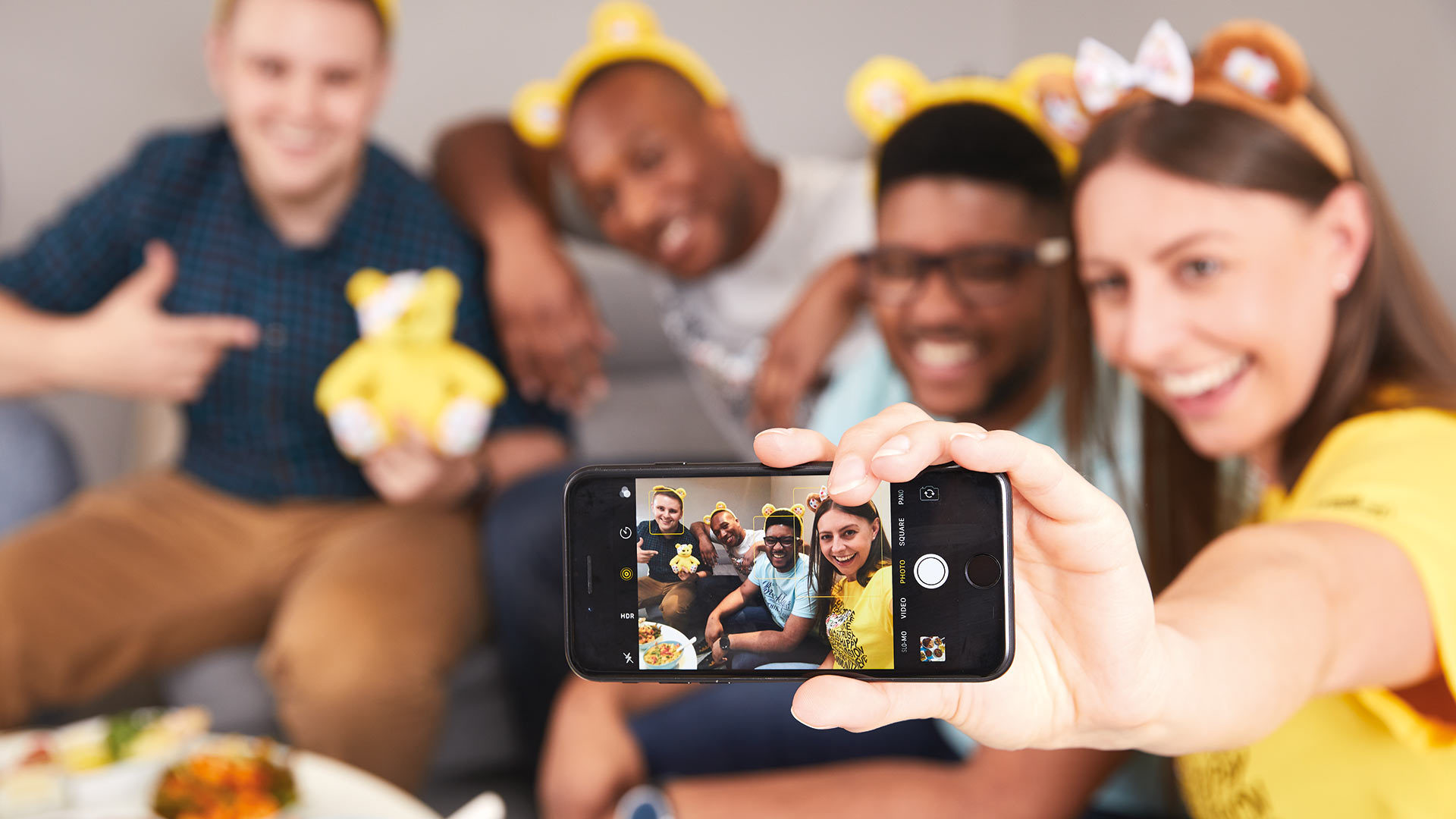 A group of friends wearing Pudsey ears taking a selfie with different curry dishes in front of them.