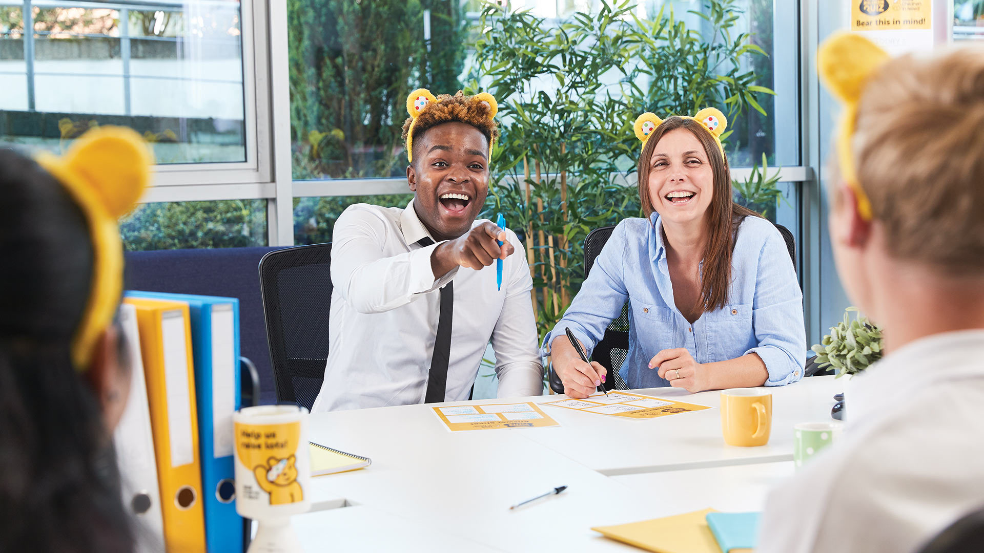 Four laughing people wearing Pudsey ears playing the big BBC Quiz in an office.