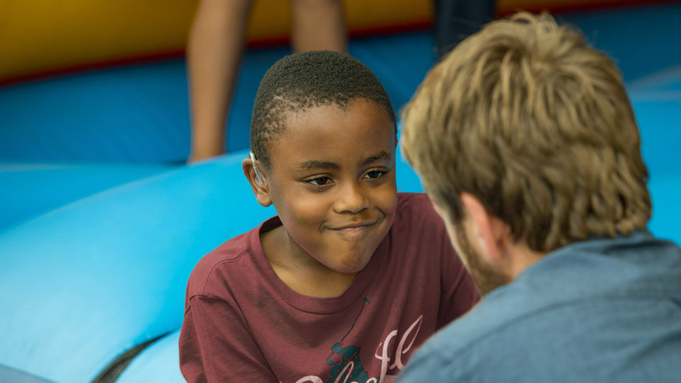 Young smiling boy wearing hearing aids engaging with a carer