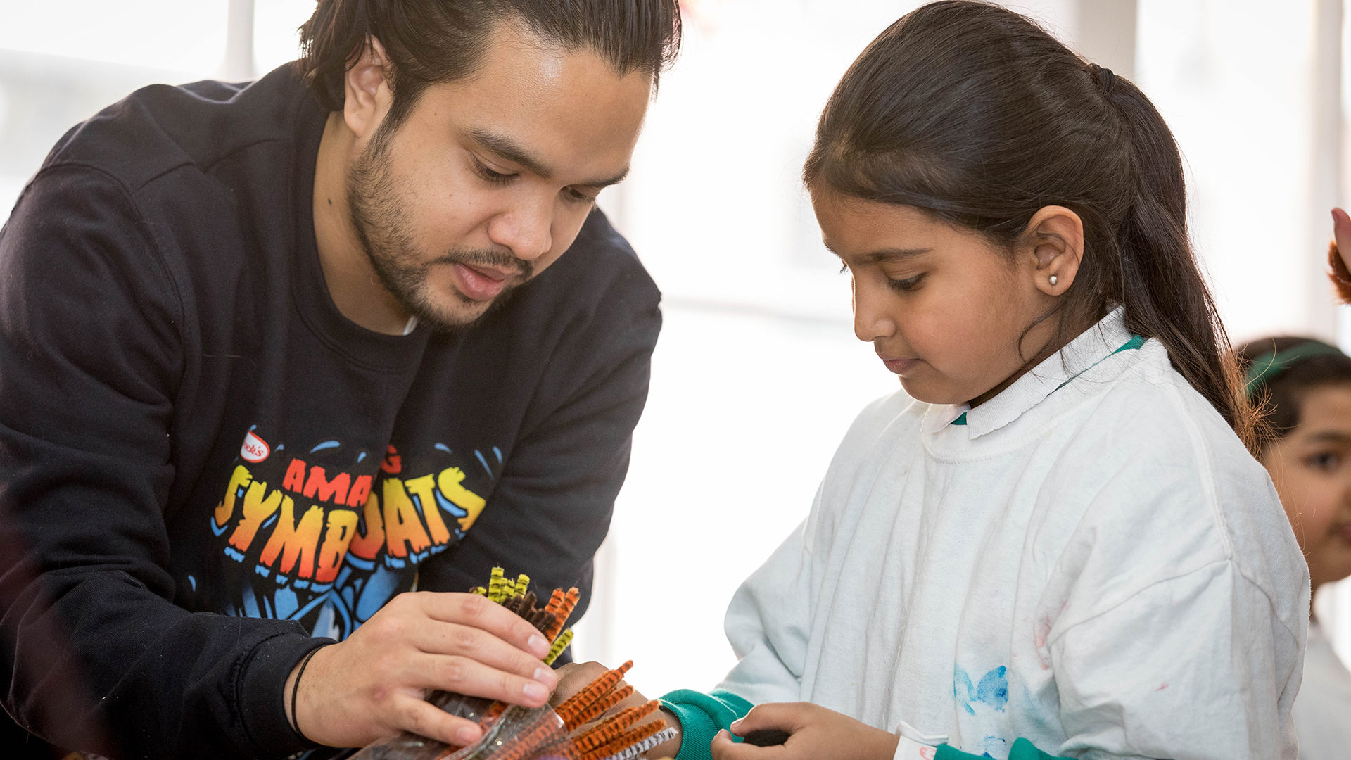 Young girl being helped to make art from colourful pipe cleaners