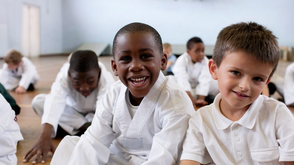 A group of smiling children wearing martial arts uniforms in a gym.