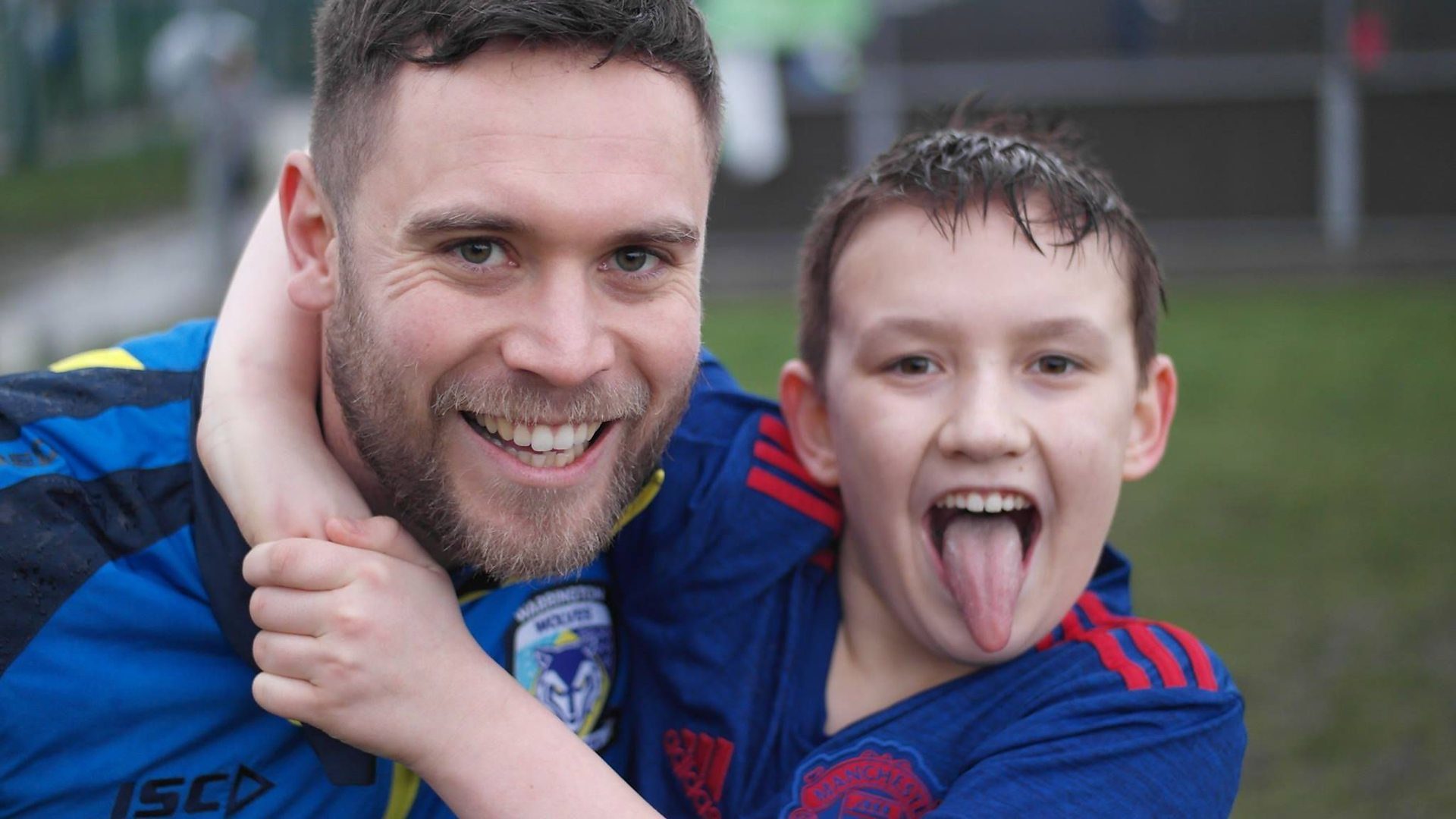 A young boy and a Warrington Wolves rugby player smiling in the rain