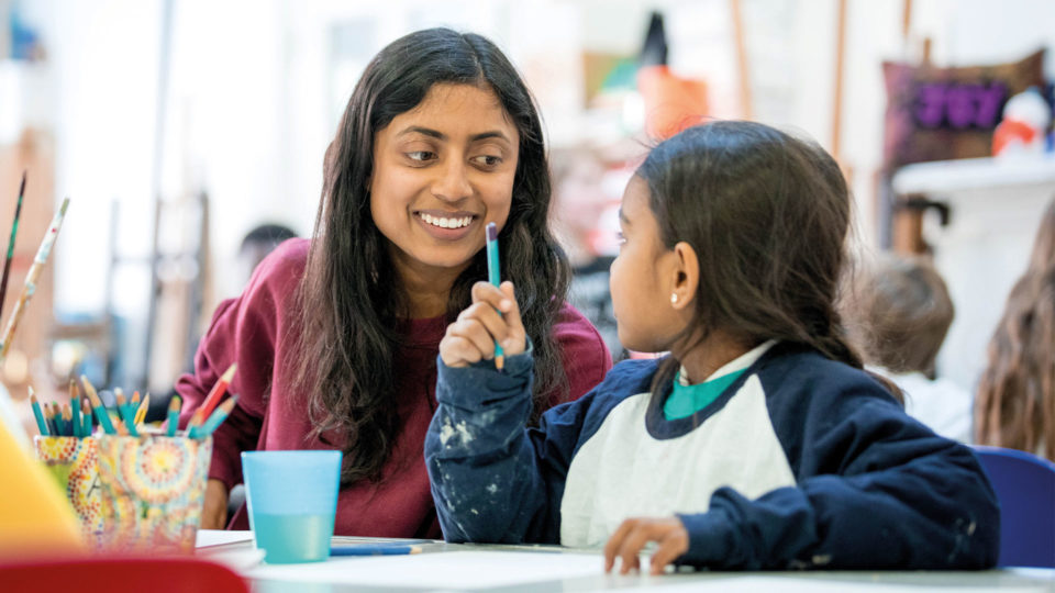 Young girl and a female volunteer smiling together in a school painting class