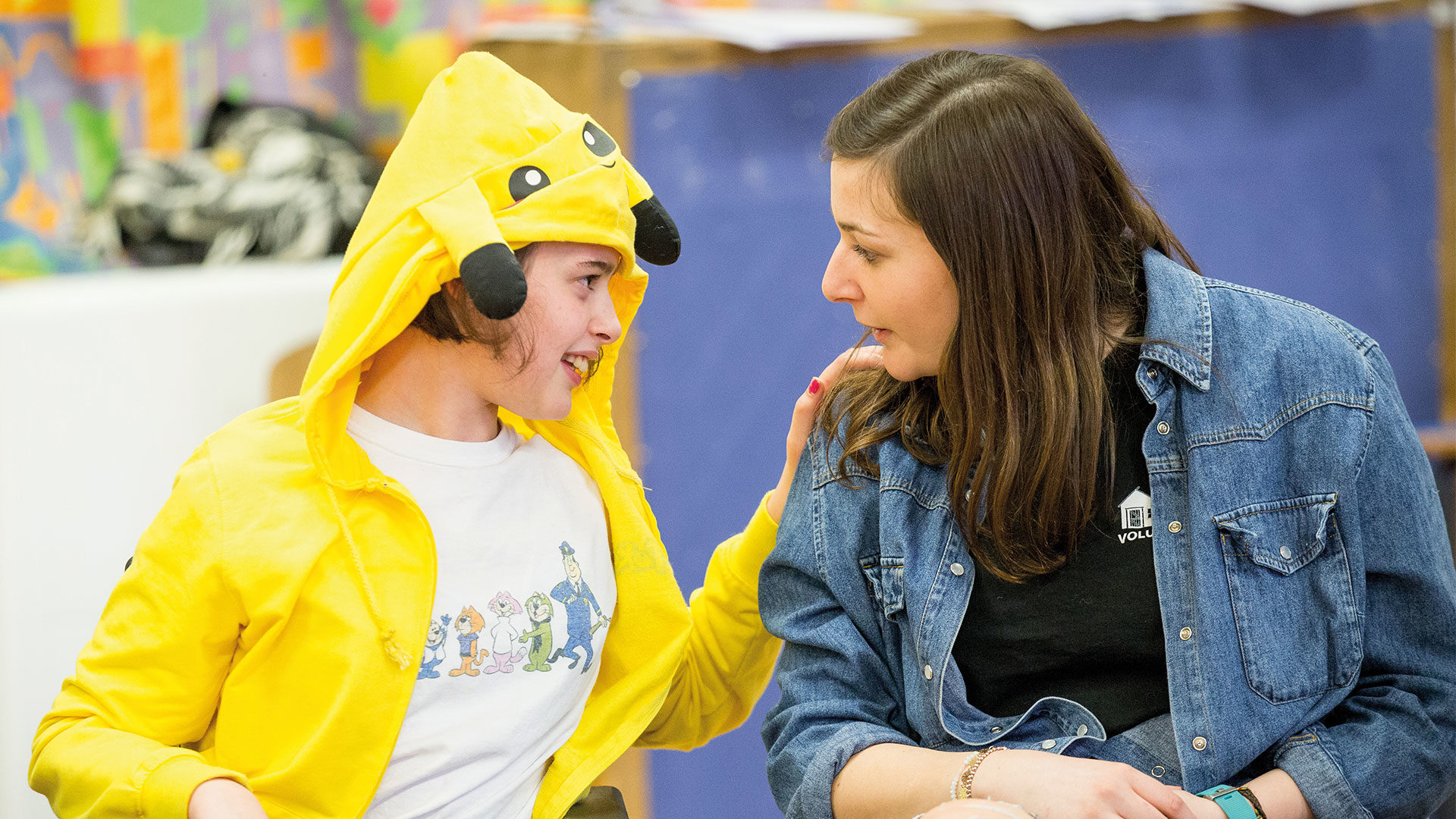 Young girl in a yellow onesie telling secrets to a female volunteer