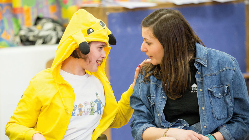 Young girl in a yellow onesie telling secrets to a female volunteer