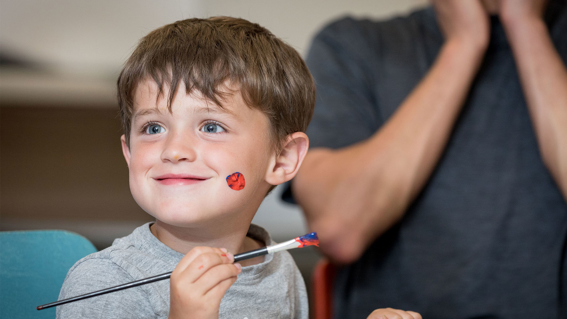 Young boy with a huge cheeky smile after painting his own face