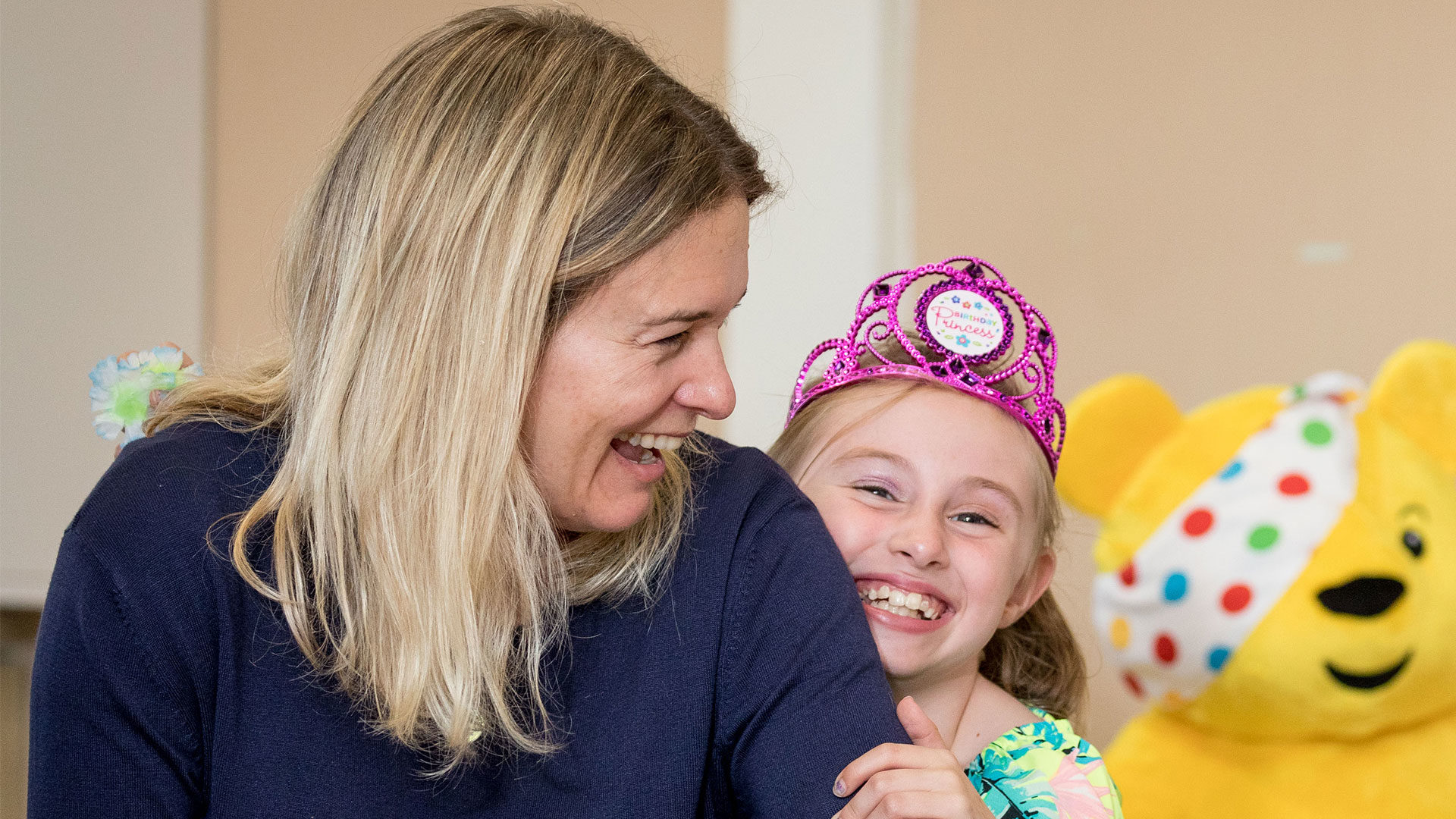 Young girl dressed as a princess hugging and laughing with a female volunteer