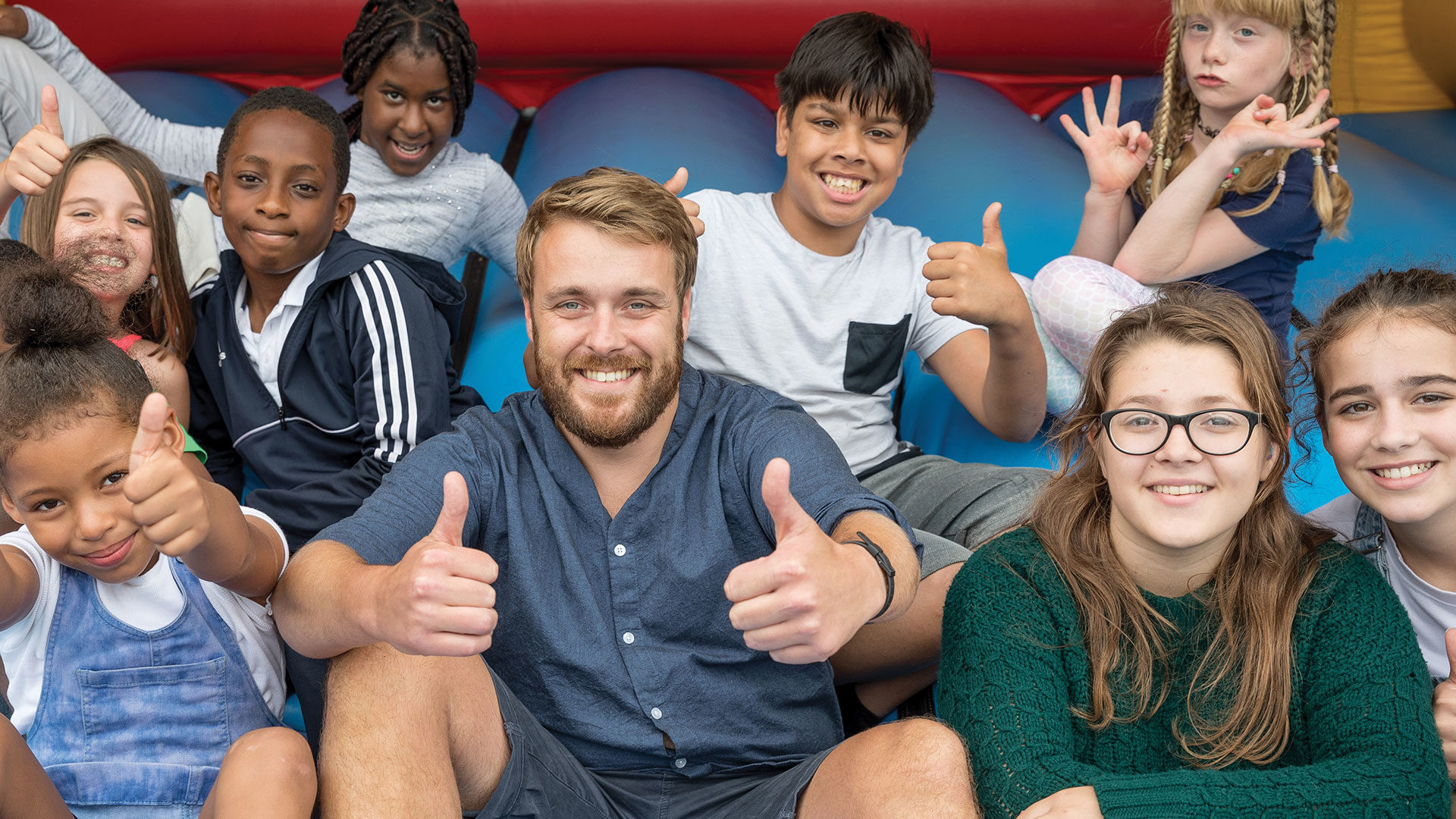 Group of children and a male volunteer, all with their thumbs up and smiling