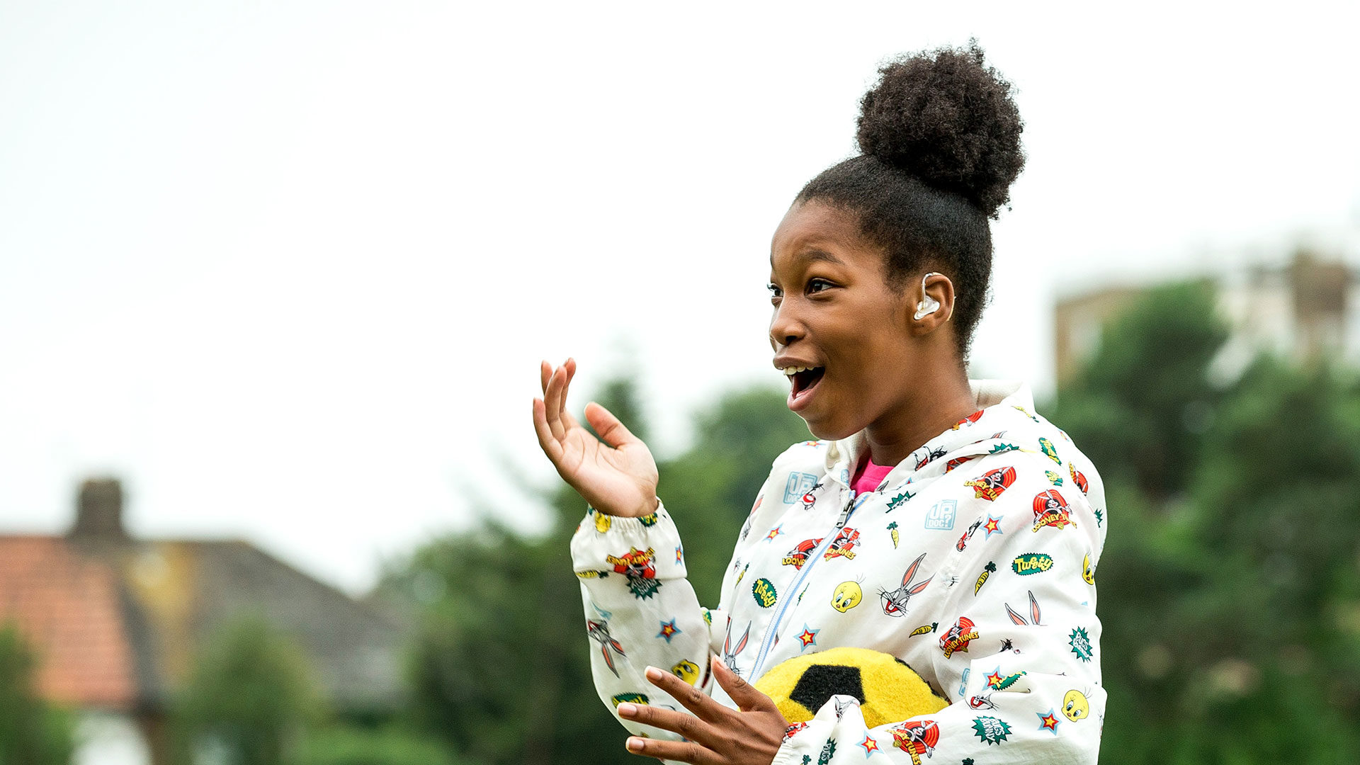 Young girl with a hearing aid holding a football laughing out loud