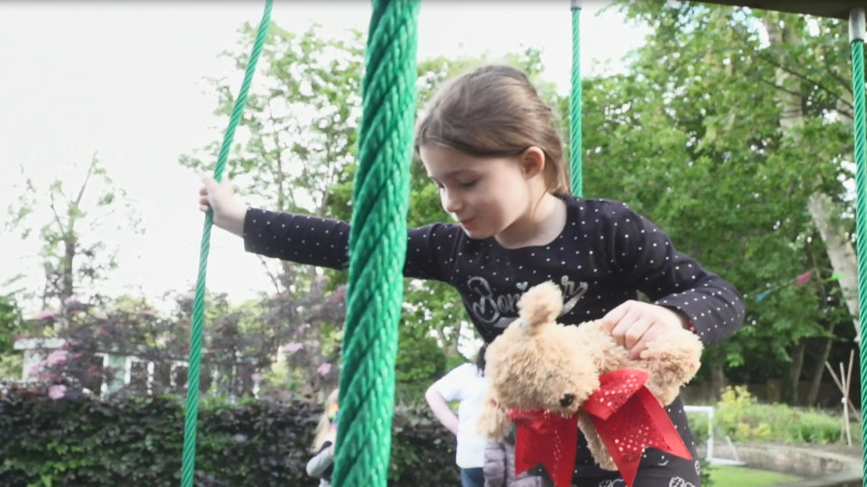 A young girl holding a teddy playing in a playground