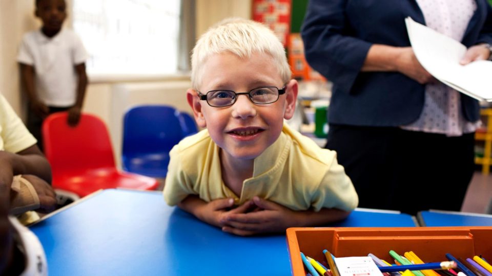 A young person leaning against a desk in a classroom