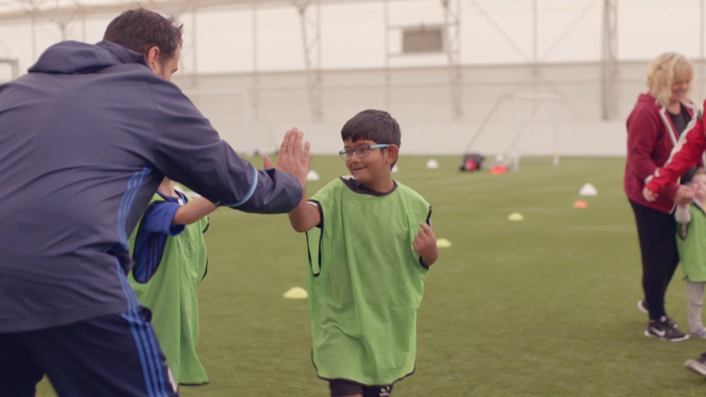 Young footballers in football kit high fiving their coach