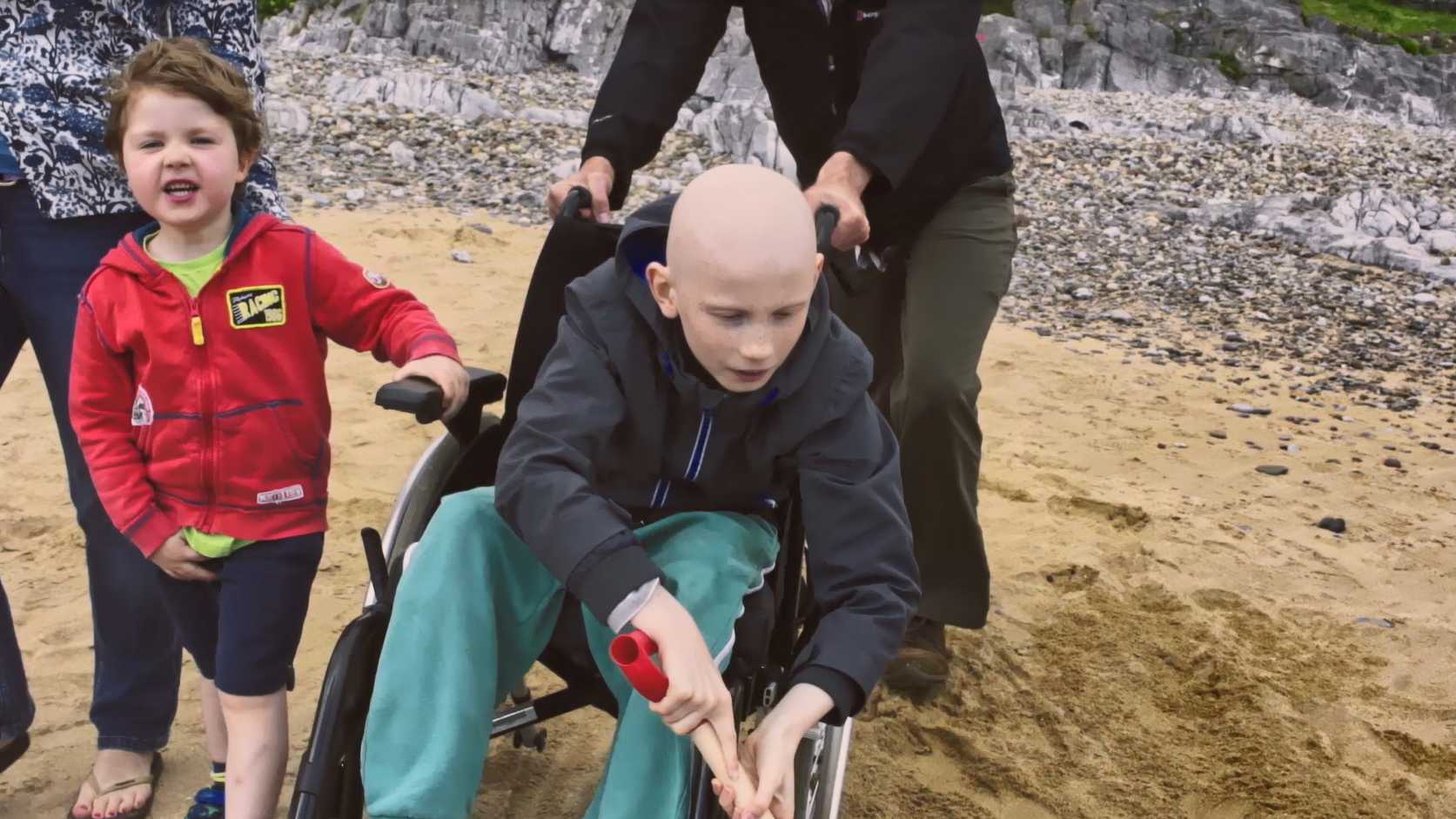 A child in a wheelchair on a beach digging in the sand with a space with his family