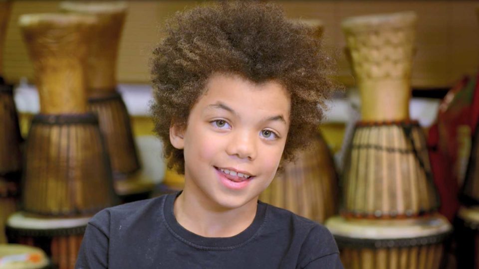 A smiling boy sat in front of percussion instruments