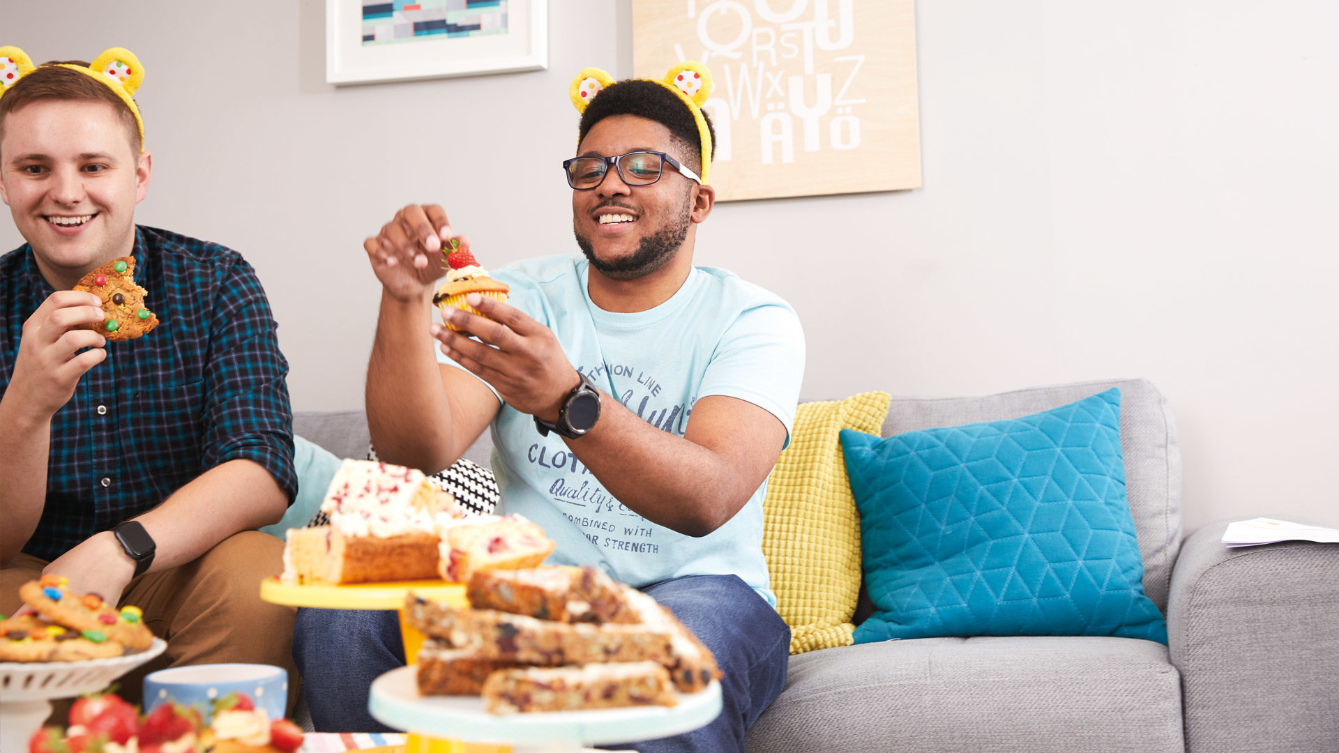 Image of two men wearing pudsey ears, one holding a cupcake the other a cookie