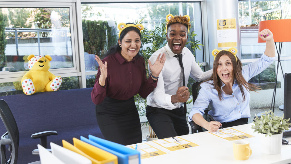 A man and two women in an office cheering and celebrating during a fundraiser