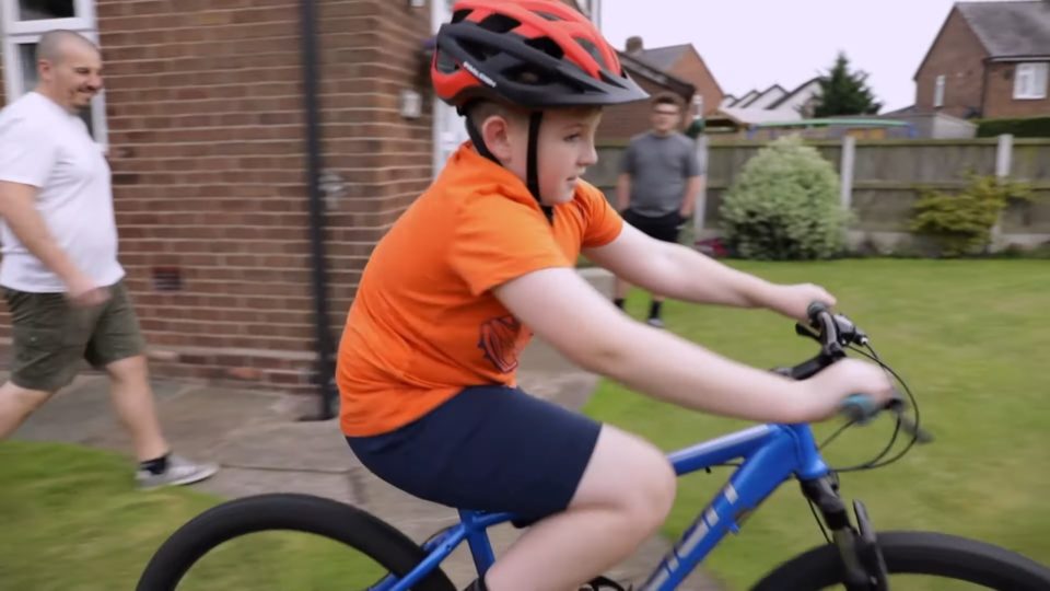 a child riding a bike in a garden weaing a helment