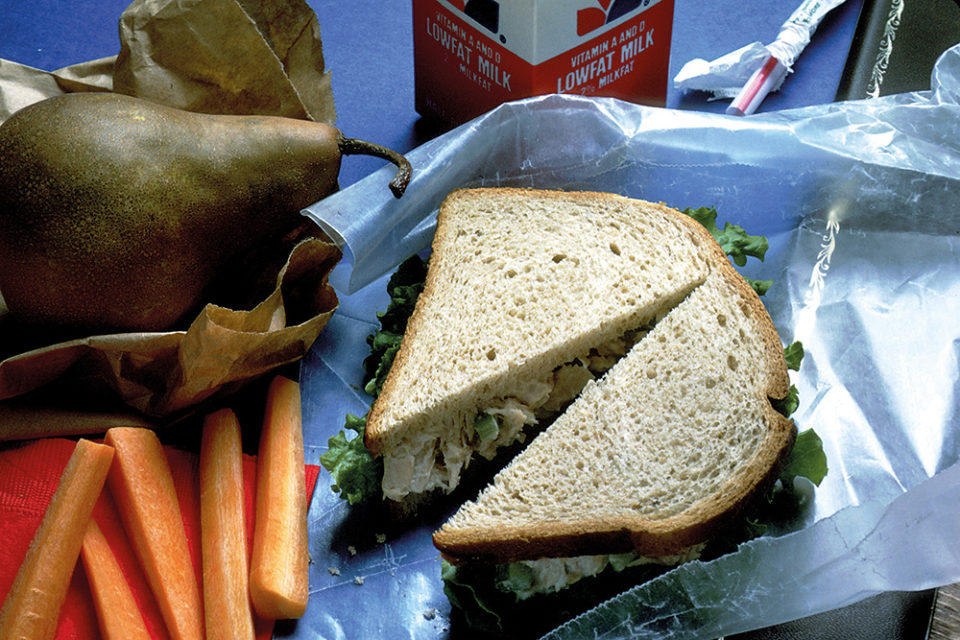 A packed lunch with a sandwich, a pear and carrots