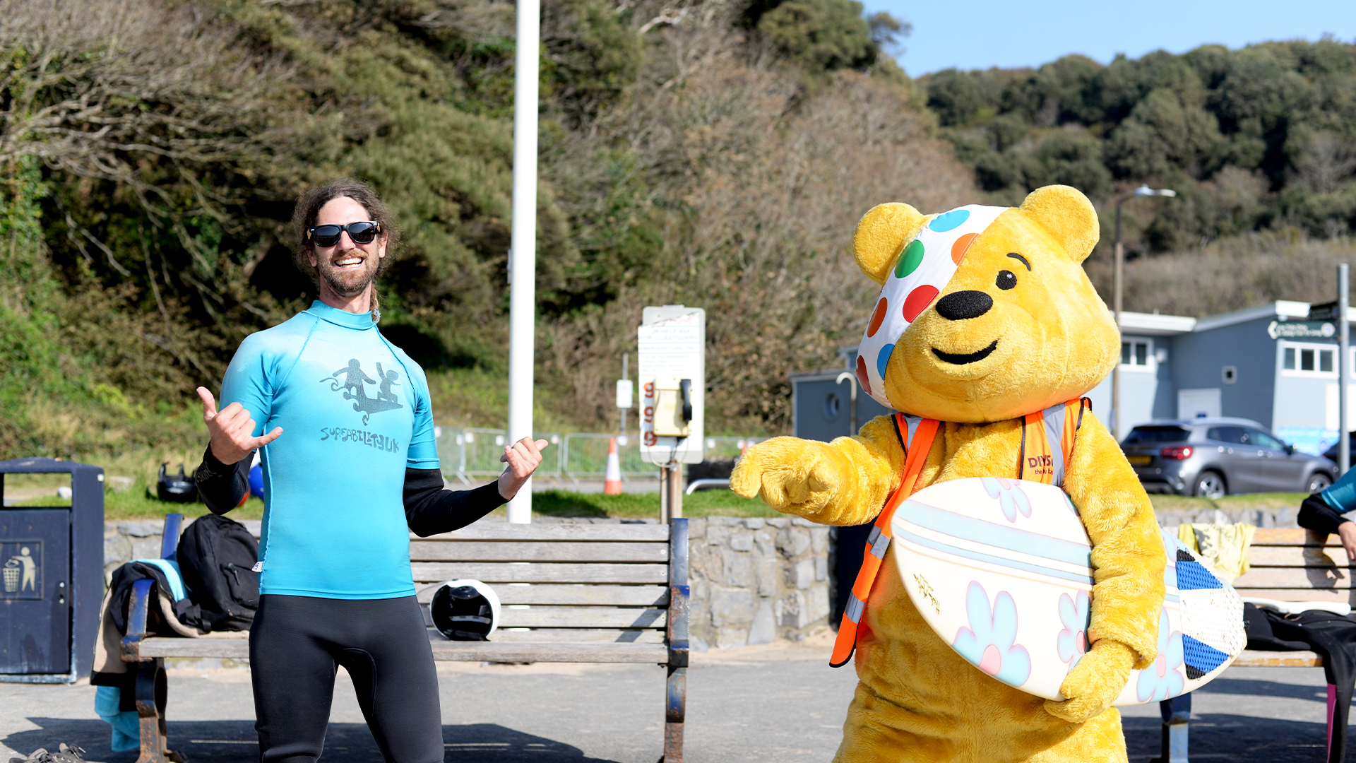 Pudsey next to a man wearing a Surfability t shirt and holding a surfboard