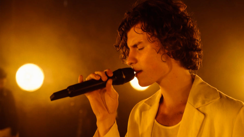 shawn mendes holding a microphone behind dramatic lighting