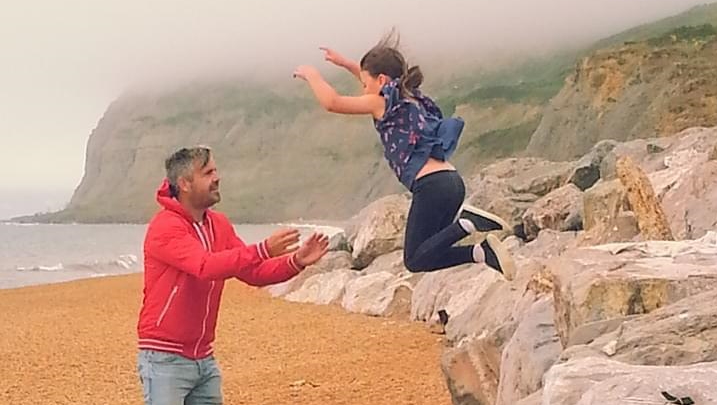 A girl jumping off a rock into a man's arms at the seaside