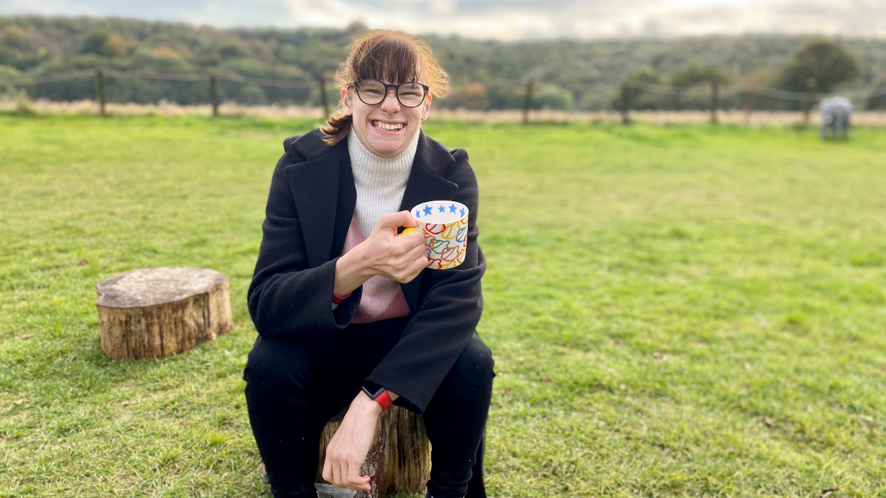 Lucy holding a mug and smiling whilst sat in a field