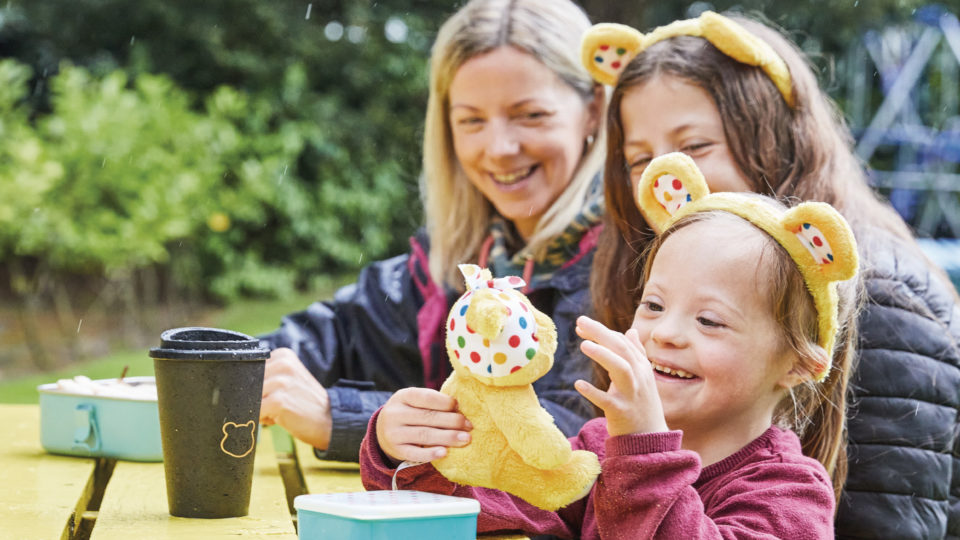 A girl holding a Pudsey and wearing ears