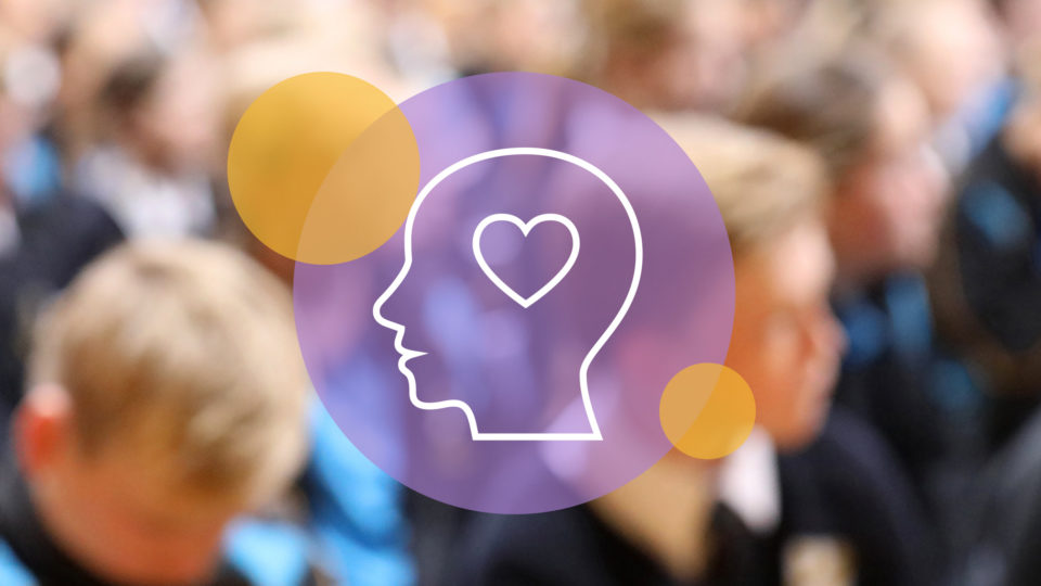 An icon of a head with a heart graphic in front of a blurred image of children