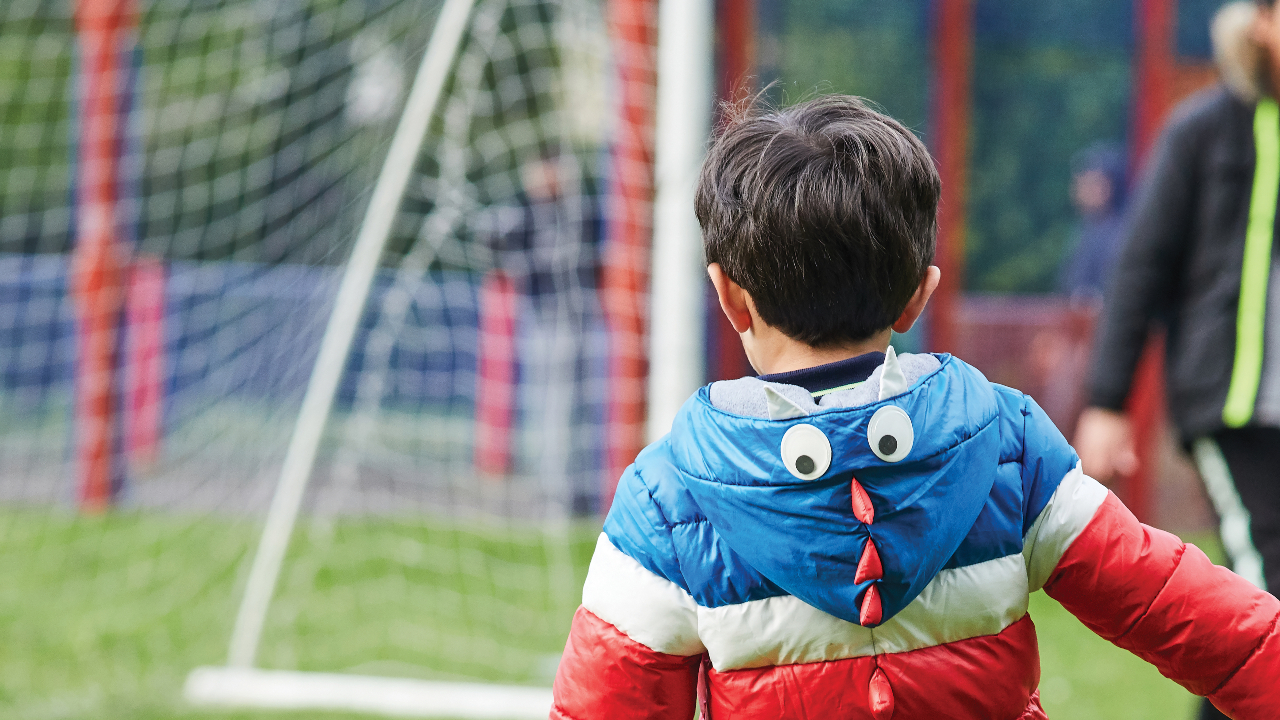 the back of a child wearing a coat. A football net is in the background