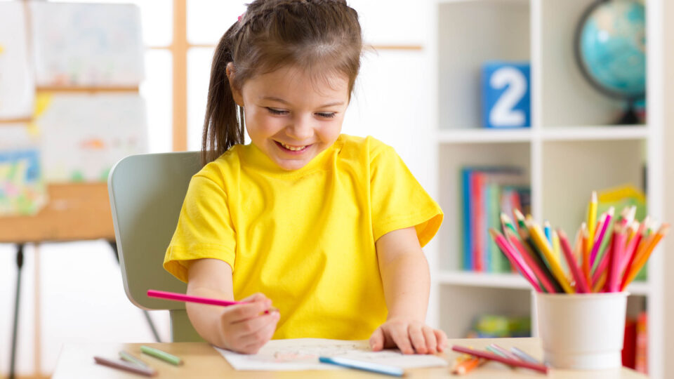 A girl wearing a yellow t-shirt drawing with a crayon