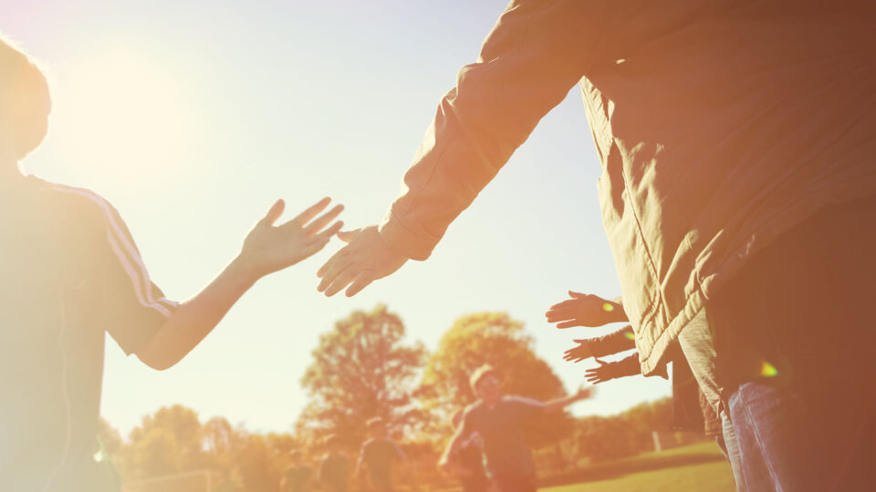 A scene in the late summer sun, with young people high-fiving a coach or teacher
