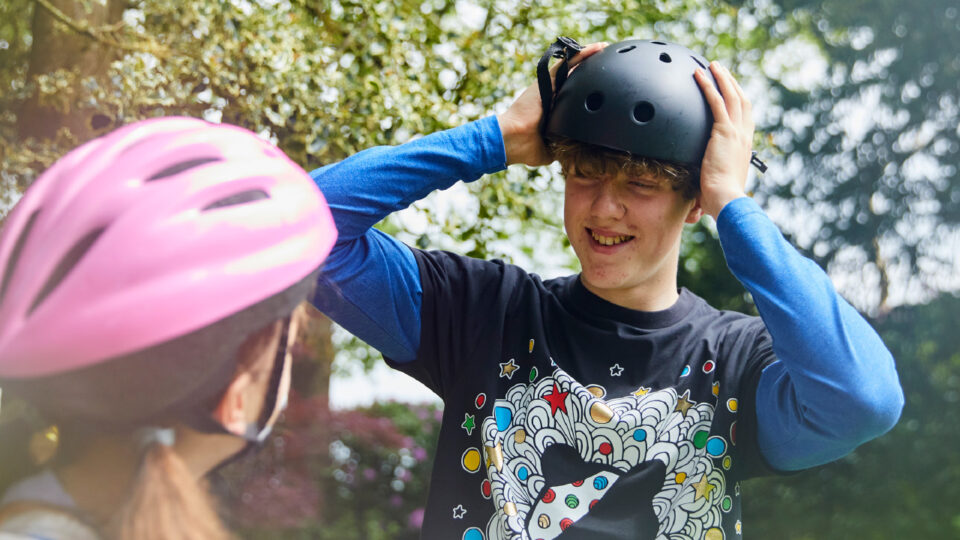 A young person wearing a Pudsey t-shirt it putting on a cycle helmet