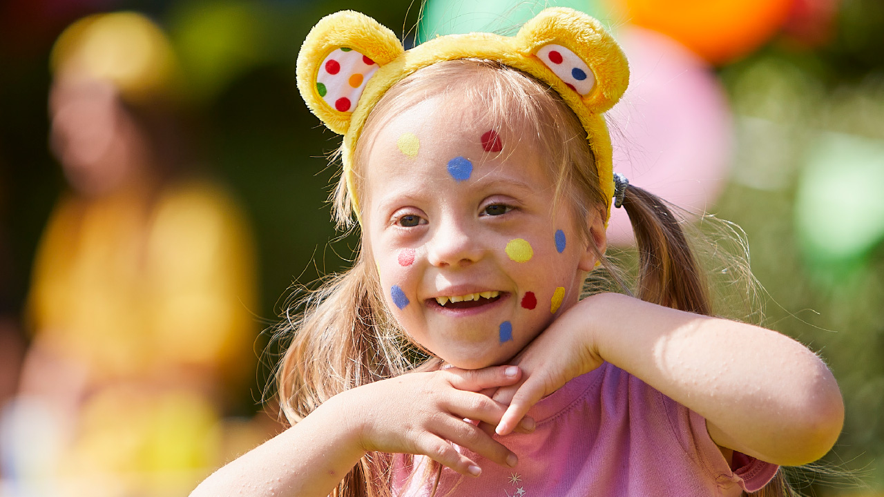A young girl smiles whilst wearing Pudsey ears and with multi-coloured face paint spots