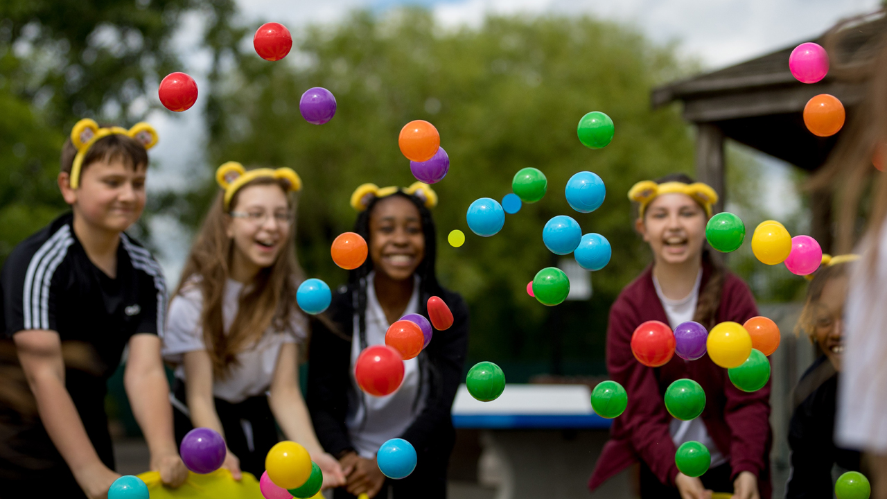 A group of children smiling, wearing pudsey ears and throwing balls