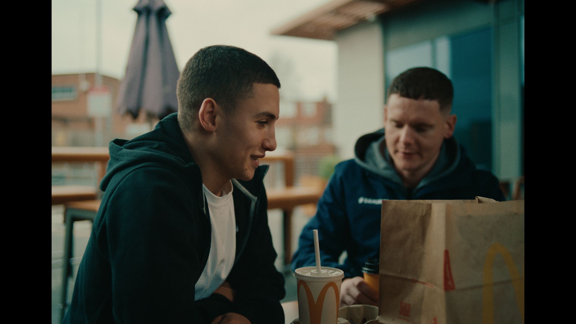 a young person and adult sat talking outside a McDonalds restaurant