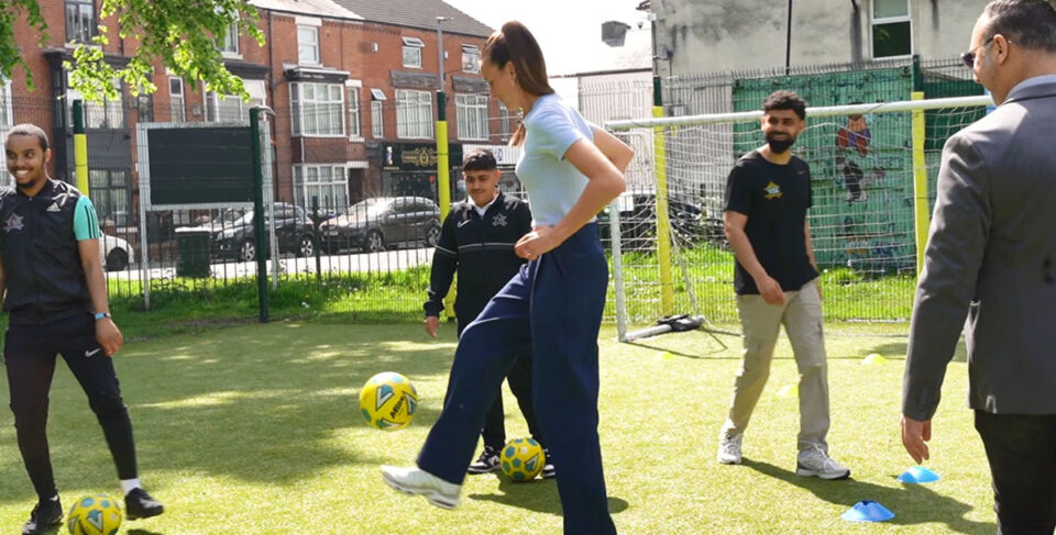 Jill Scott playing football in a field with youth workers
