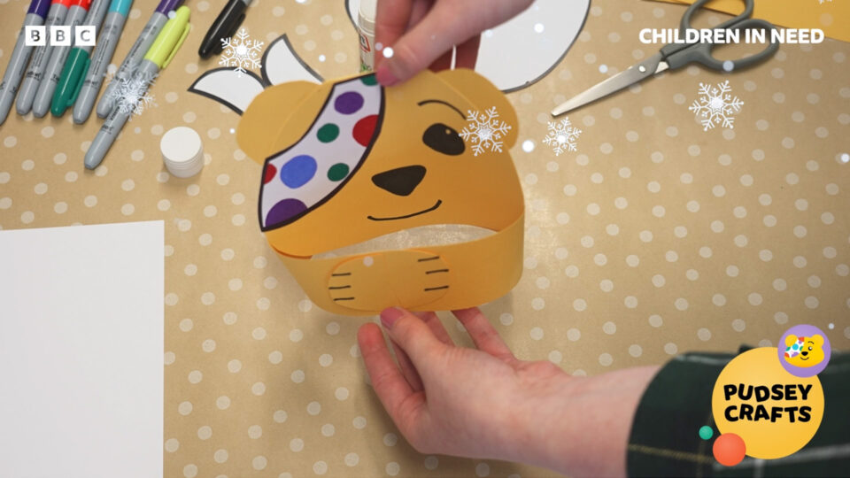 A screenshot from the craft video showing yellow card cut into a Pudsey bear shape, with the arms wrapping as if in a hug