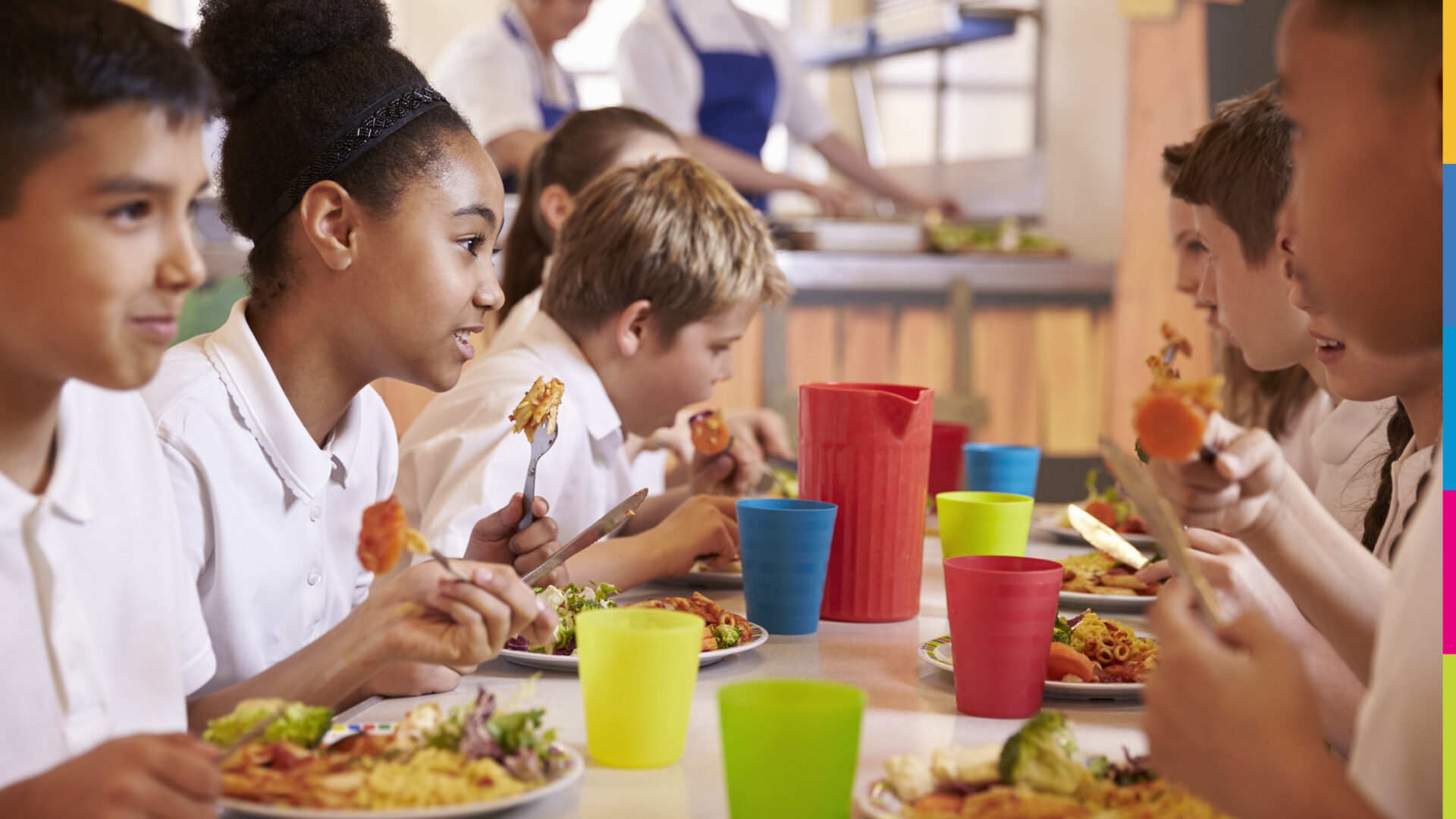 a group of school children sat around a table together eating and drinking