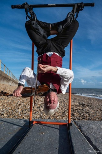 A man playing the violin upside down on a swing
