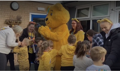 Pudsey with a group of smiling children and adults wearing yellow