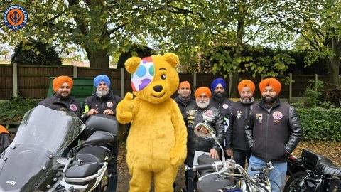 A group of people with motorbikes behind a Pudsey with a thumbs up