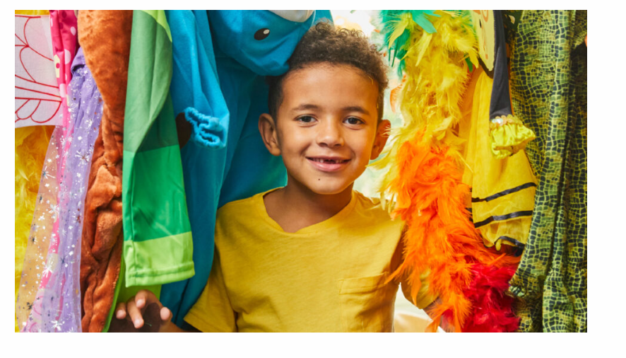 a young boy in a yellow t-shirt surrounded by clothes
