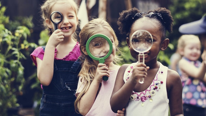 Three young children playing with magnifying glasses
