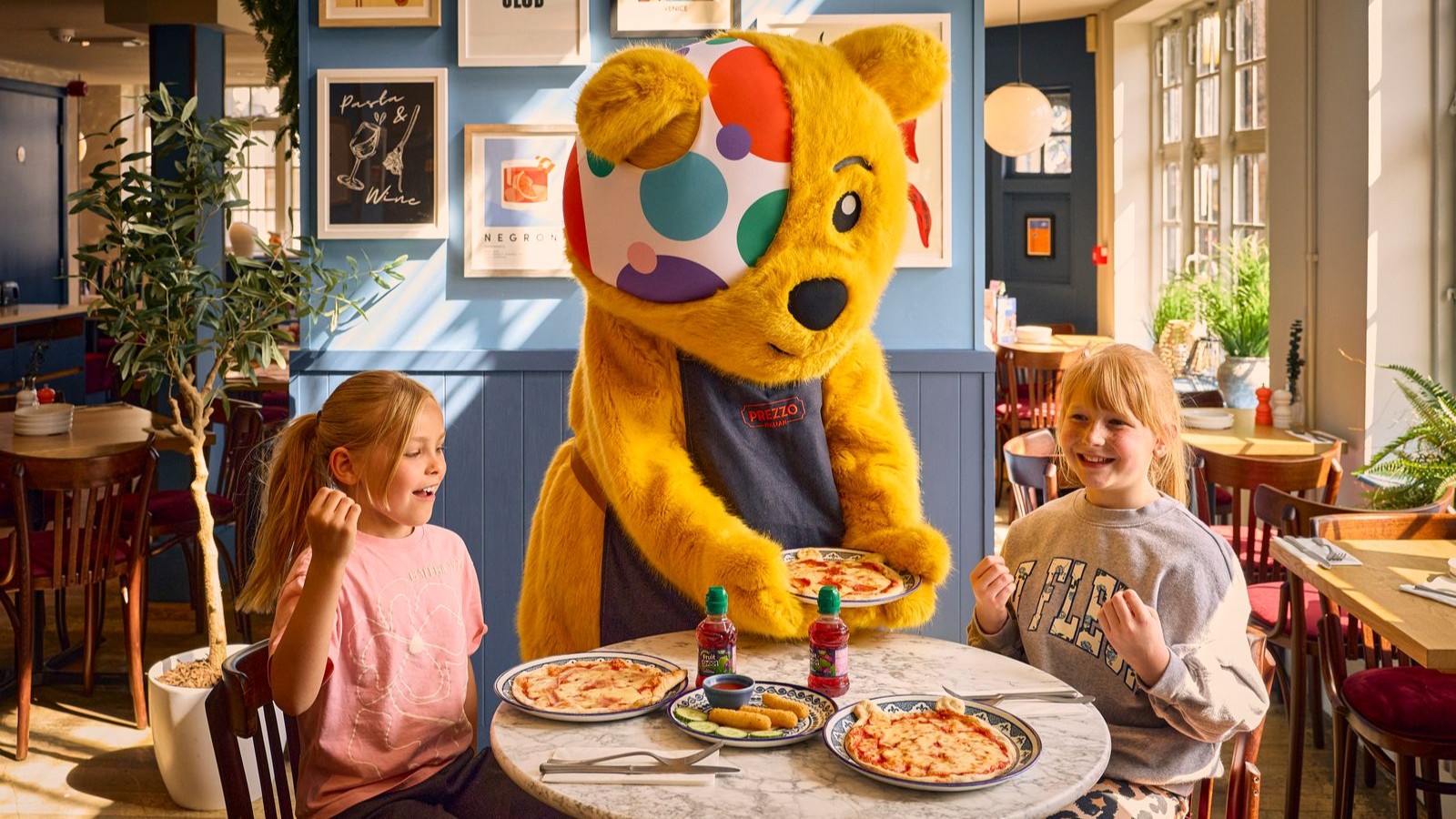 Pudsey serving a Pizza to two children in a prezzo restaurant. The children are excited