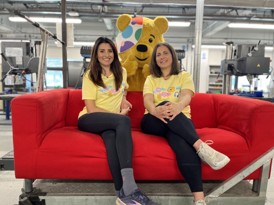 Two ladies on a red sofa with Pudsey standing behind them